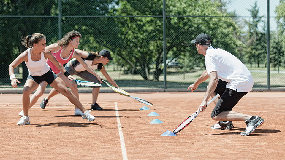 Tennis players training, running to touch cones, while coach instructs them.
